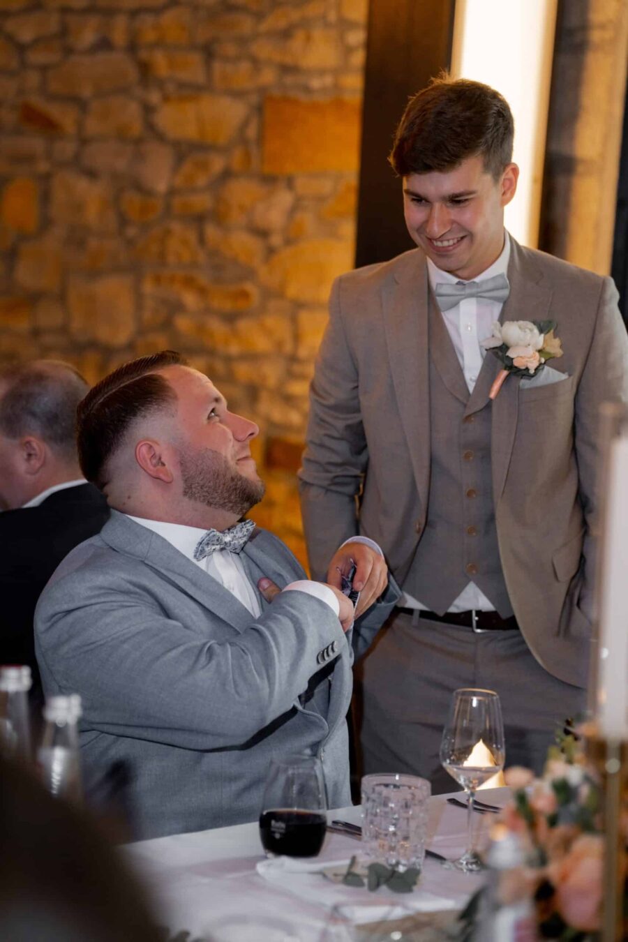 Gäste in grauen Anzügen bei Hochzeitsfeier am Tisch