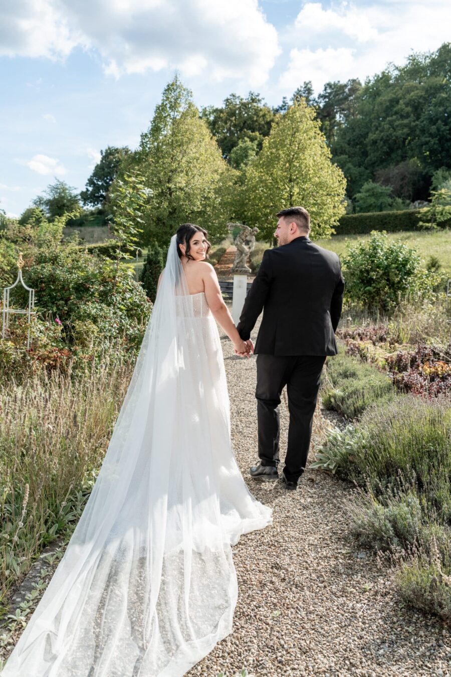 Brautpaar im Garten auf Kiesweg händchenhaltend