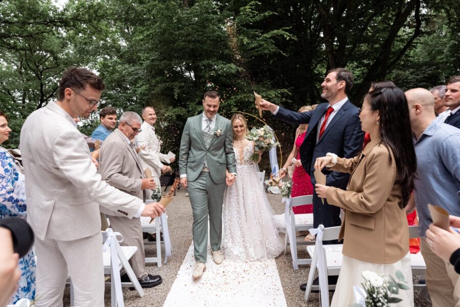 Hochzeitspaar schreitet durch Spalier von Gästen im Freien
