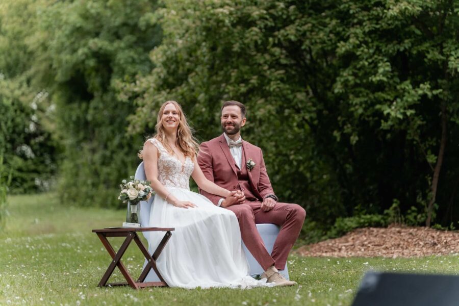 Brautpaar sitzt lächelnd im grünen Garten