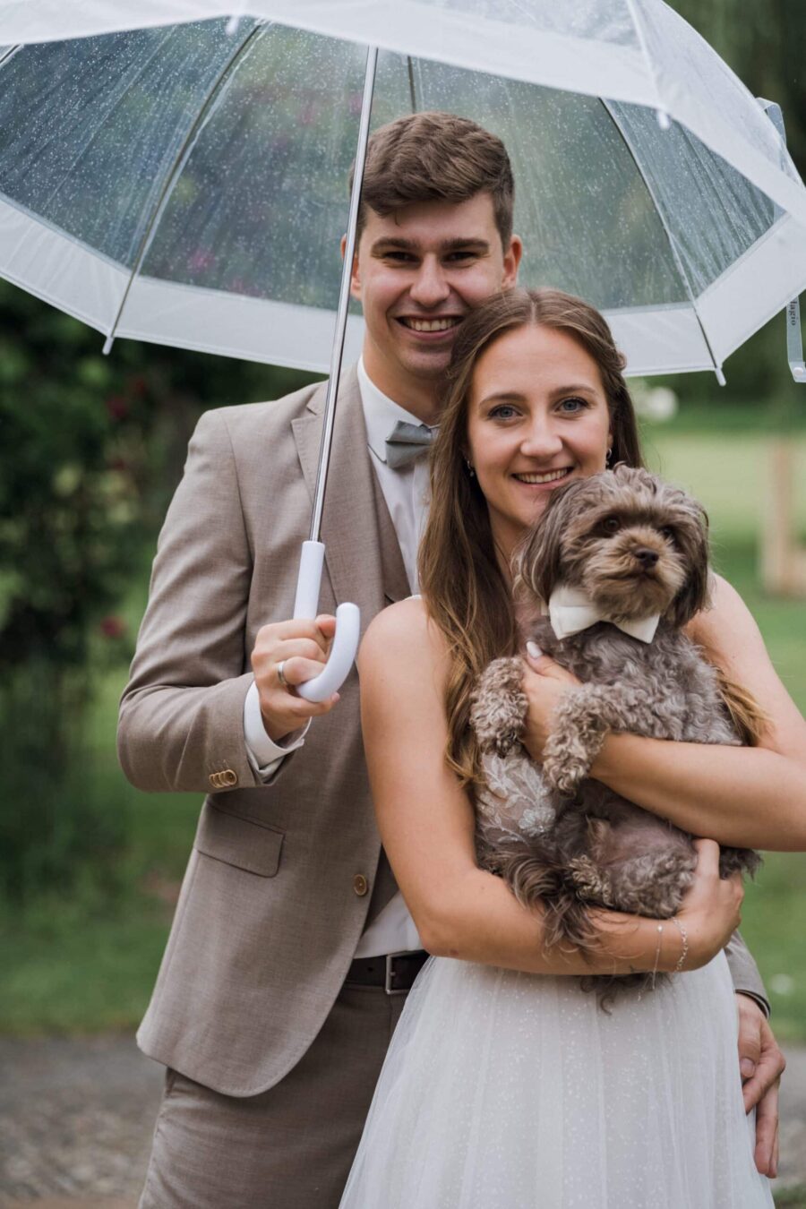 Brautpaar mit Hund unter Regenschirm im Garten