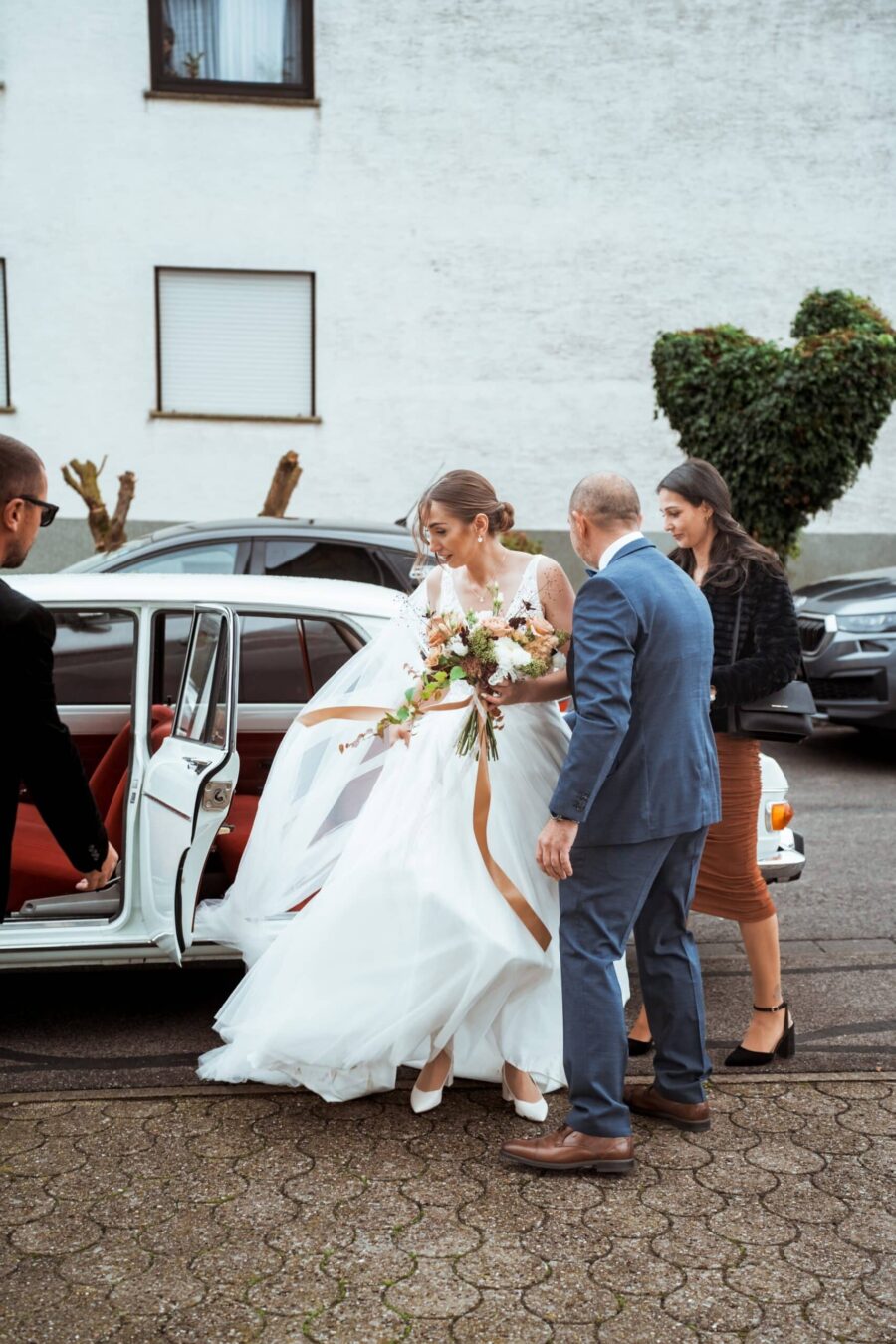 Braut steigt aus dem Hochzeitsauto mit Brautstrauß