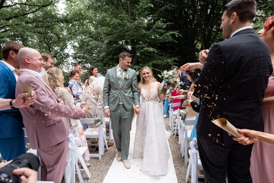 Brautpaar im Freien, von Gästen mit Blüten bejubelt.