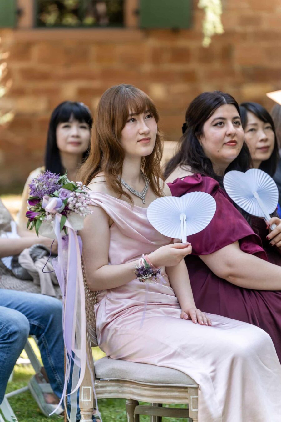 Gäste in festlicher Kleidung mit Fächern, SommerhochzeitHofgut Hünersdorff