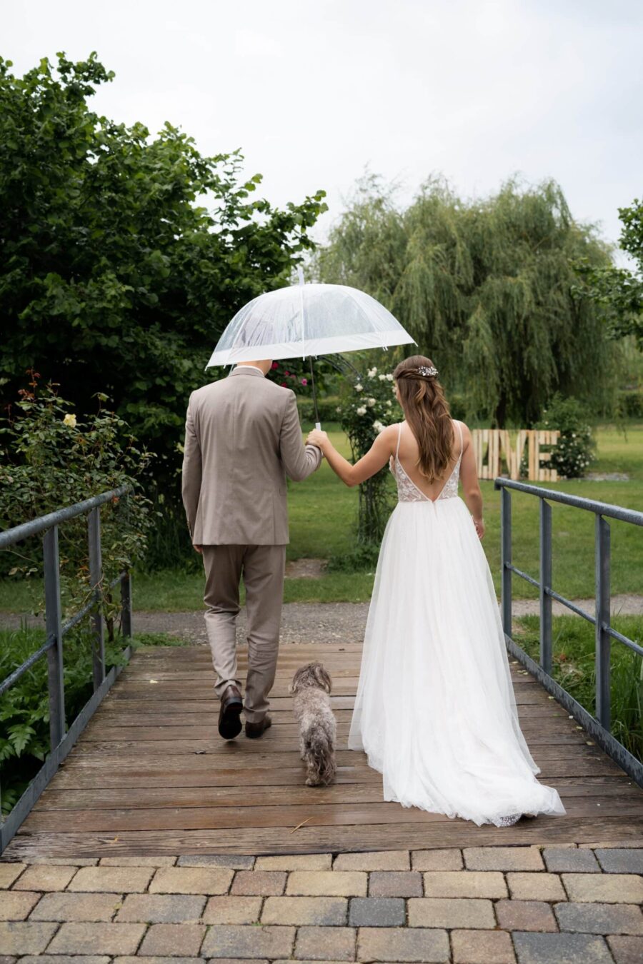 Brautpaar mit Regenschirm und Hund im Garten