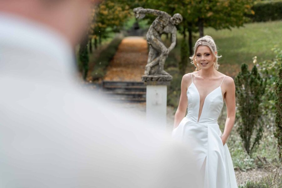 Braut im weißen Kleid vor Gartenstatue