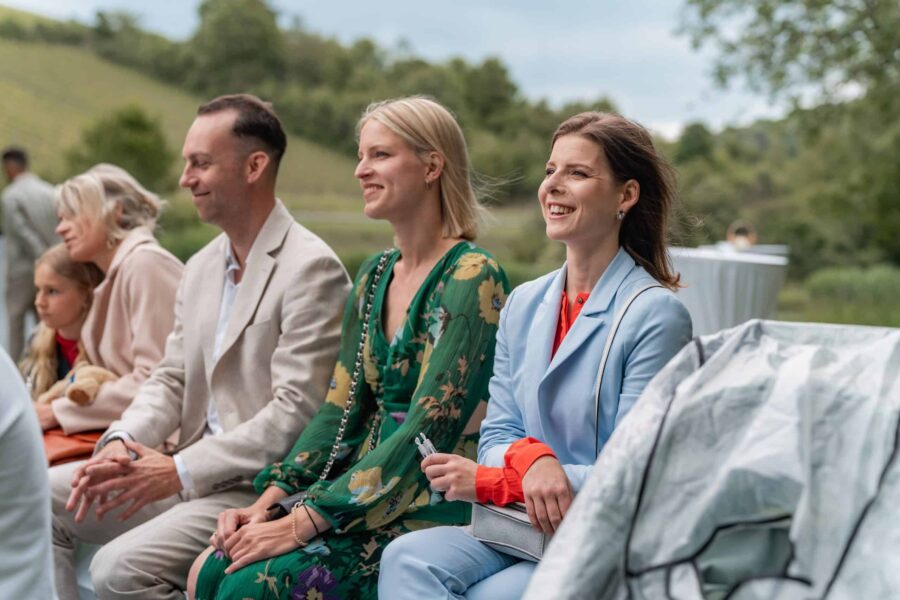 Hochzeitsgäste im Freien lächelnd auf Sitzbänken