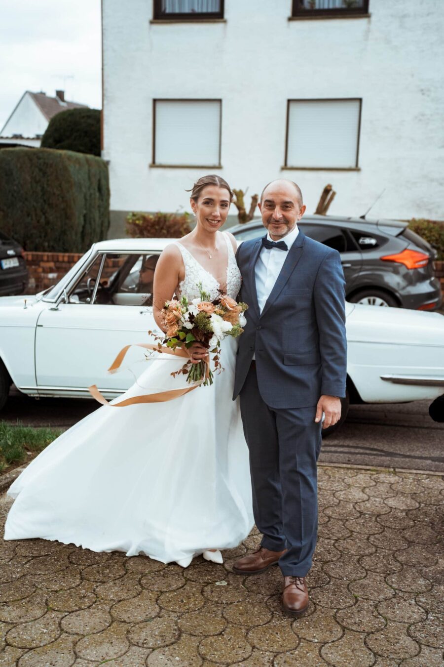 Brautpaar vor weißem Hochzeitsauto im Freien