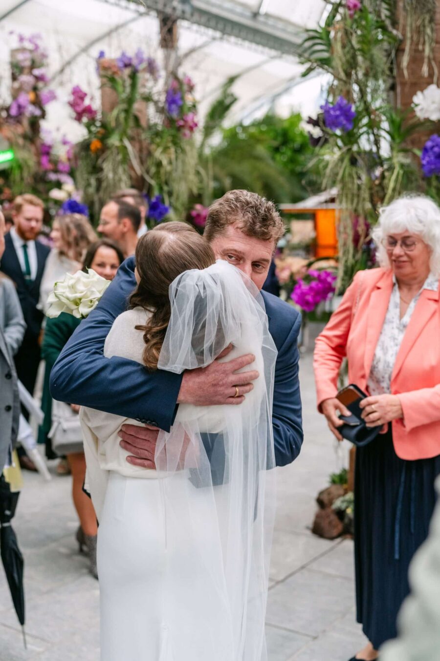 Hochzeit Insel Mainau Bodensee – Heiraten am Bodensee 212 Braut umarmt Gratulanten im blumengeschmückten Garten