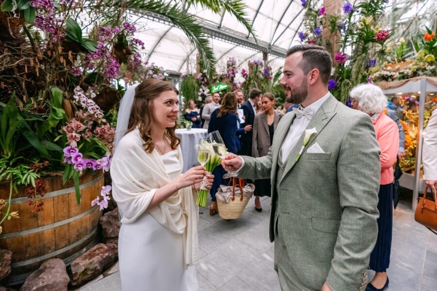 Brautpaar stößt mit Sekt an im botanischen Gewächshaus