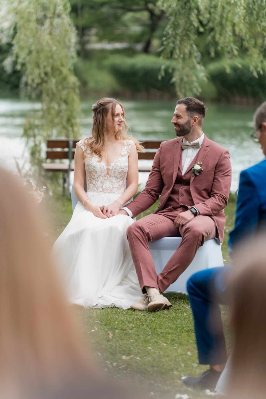 Brautpaar sitzt lachend am See im Garten