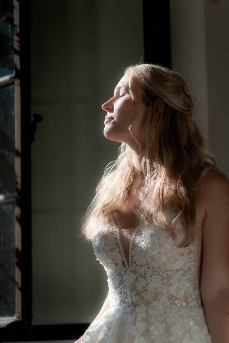 Braut im Sonnenlicht am Fenster.