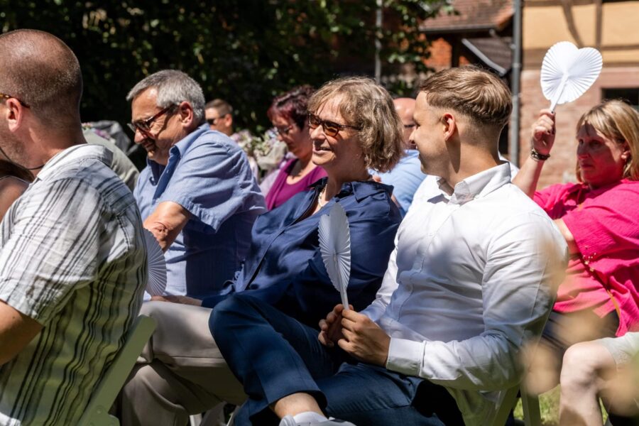 Gäste mit Fächern im Freien, Sonne, Lachen. Hofgut Hünersdorff