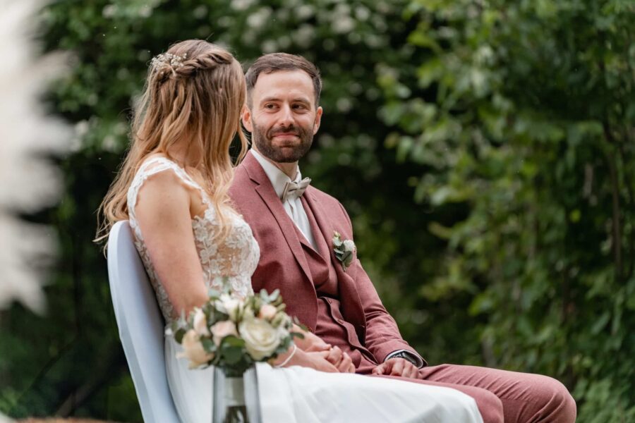 Brautpaar sitzt im Garten auf weißen Stühlen