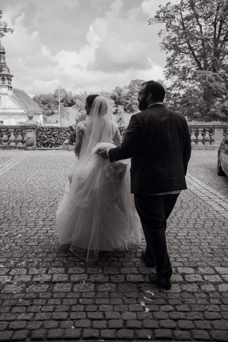 Brautpaar geht Hand in Hand über Kopfsteinpflaster.