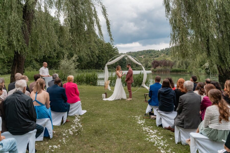 Outdoor-Trauung am See mit Gästen und Blumenschmuck