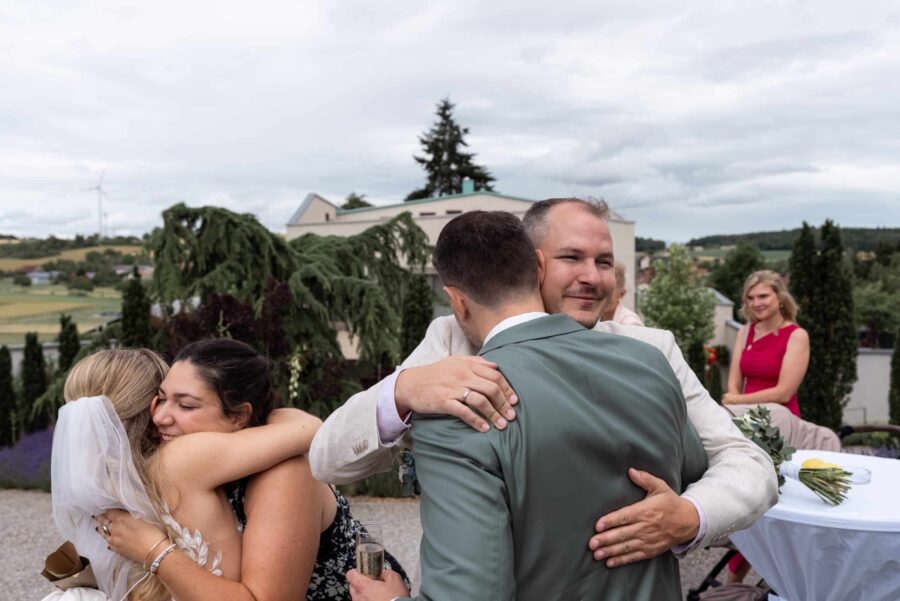Gäste umarmen sich bei Hochzeitsempfang im Freien
