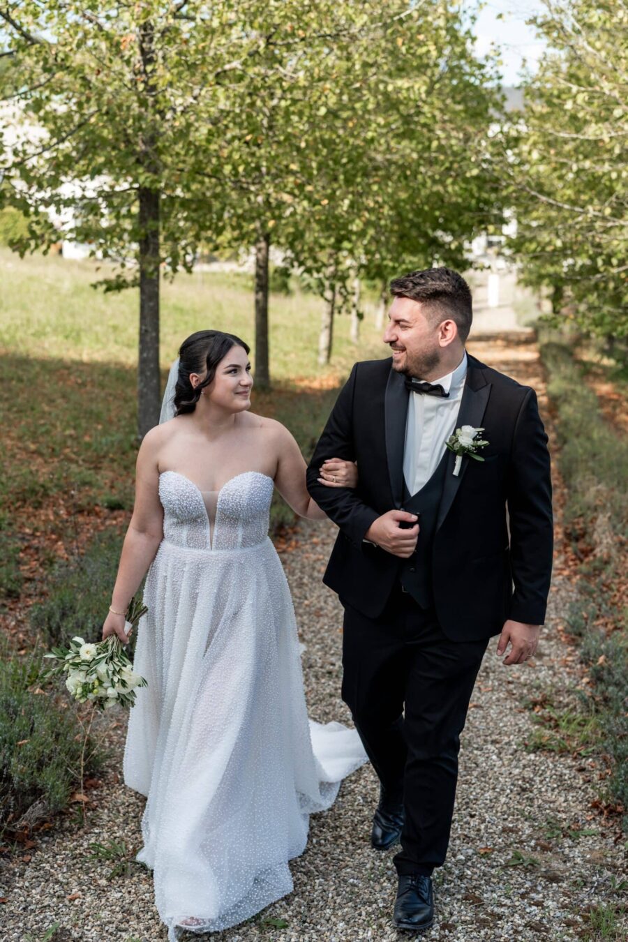 Brautpaar spaziert lächelnd im grünen Gartenweg