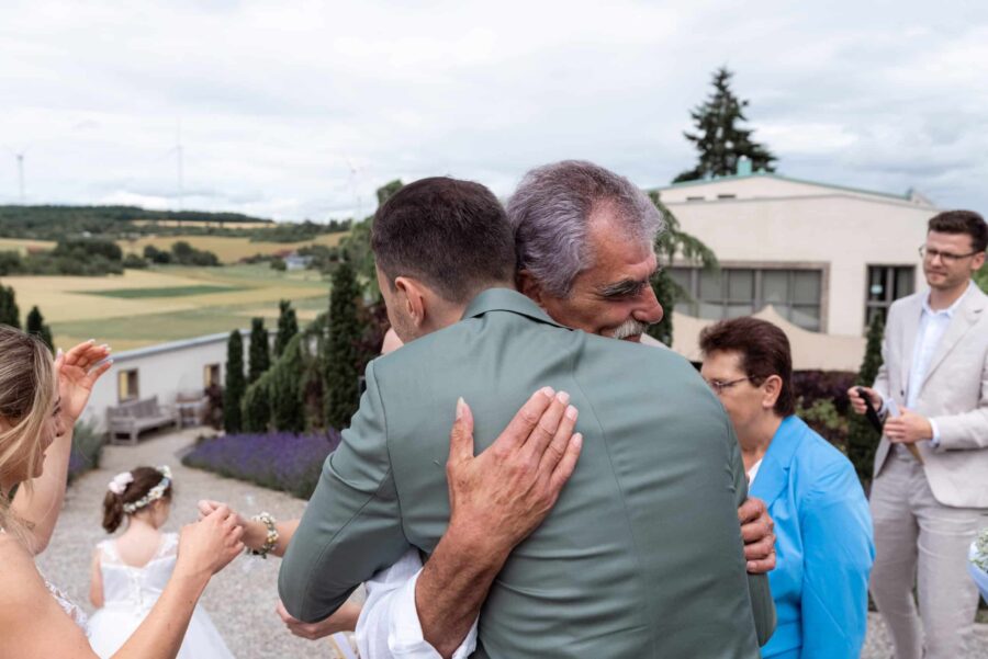 Umarmung bei Hochzeit im Freien mit Gästen.