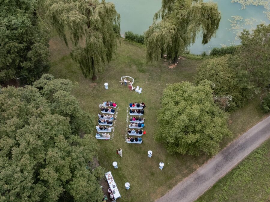 Freilufttrauung am See mit Gästen im Garten.