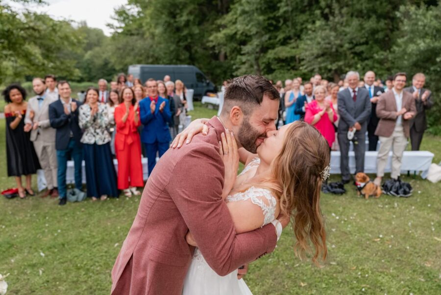 Brautpaar küsst sich vor applaudierenden Gästen.