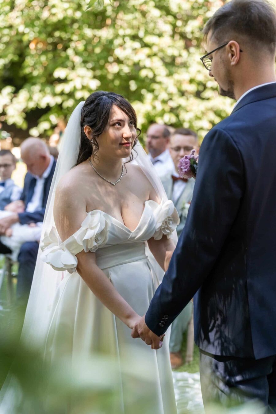 Brautpaar bei Trauung im Garten, Gäste im Hintergrund. Hofgut Hünersdorff