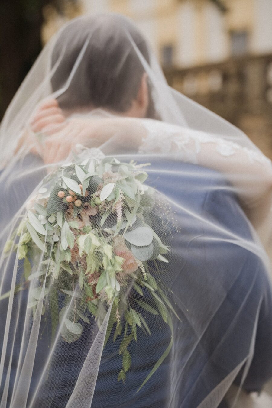 Brautpaar unter Schleier mit Blumenstrauß
