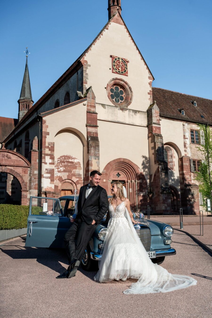 Brautpaar vor historischer Kirche mit Oldtimer