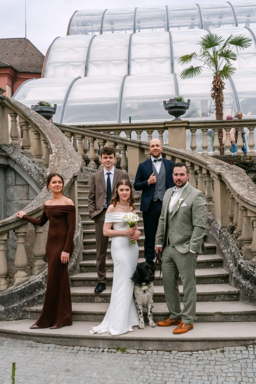 Hochzeit Insel Mainau Bodensee – Heiraten am Bodensee 229 Brautpaar mit Gästen und Hund auf Treppe am Gewächshaus