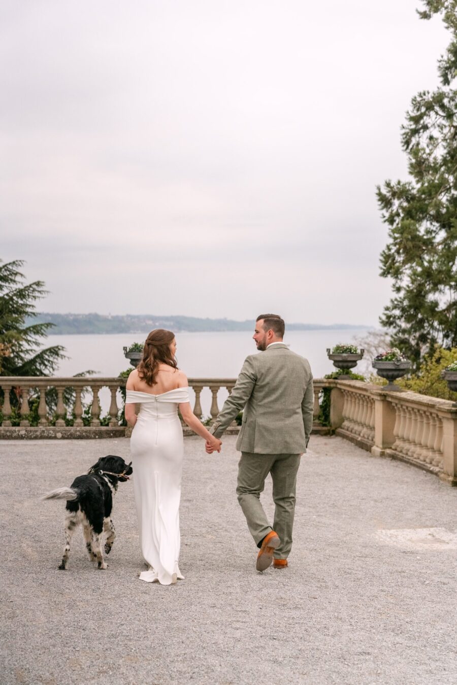 Hochzeit Insel Mainau Bodensee – Heiraten am Bodensee 230 Brautpaar spaziert mit Hund auf Terrasse am See
