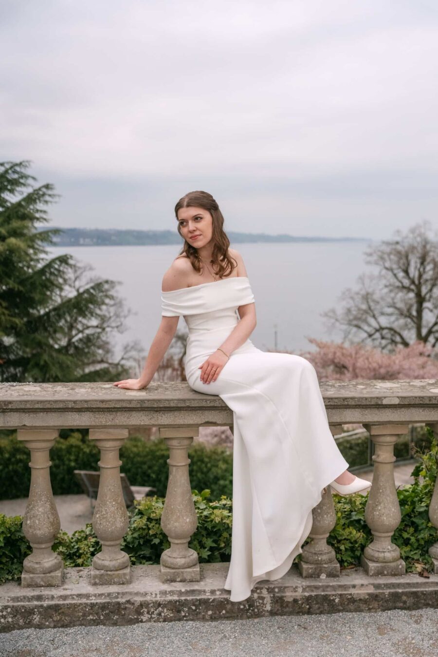 Braut im weißen Kleid an Steinbalustrade mit Seeblick