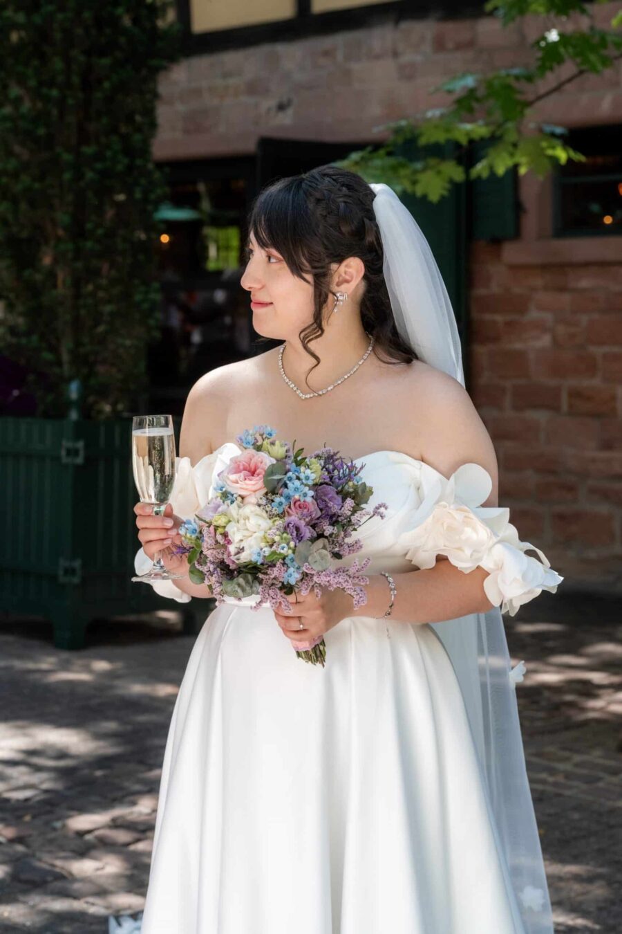 Braut mit Blumenstrauß und Sektglas im Hofgarten Hofgut Hünersdorff