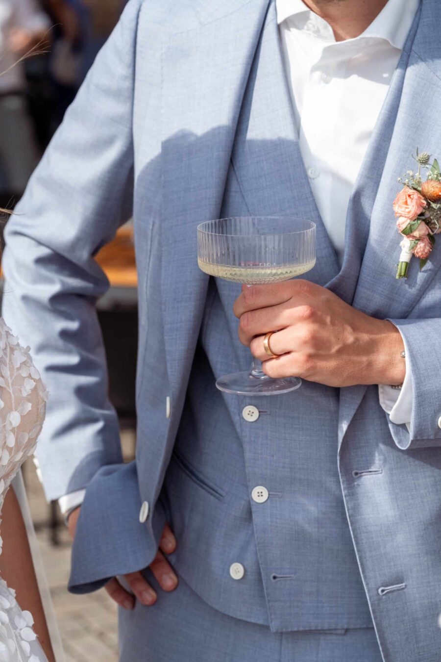 Bräutigam hält Champagnerglas und Blumenanstecker