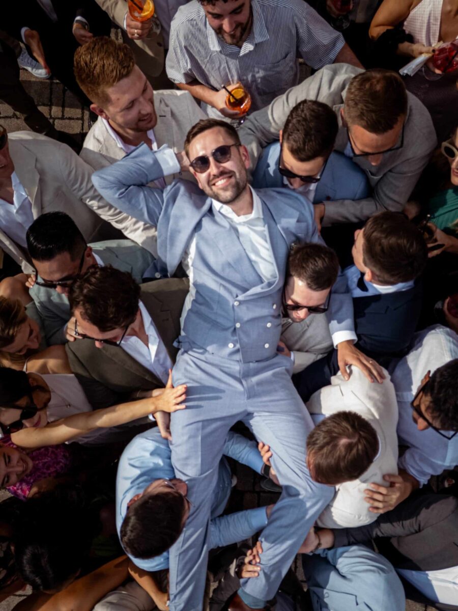 Hochzeit Steinburg Würzburg | Editorial Style & Party | Florian Knusper 149 Mann in Anzug wird von Gästen hochgehoben.