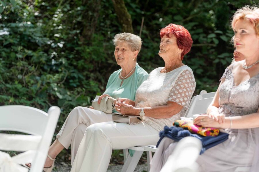 Hochzeitsgäste sitzen im Freien auf weißen Stühlen