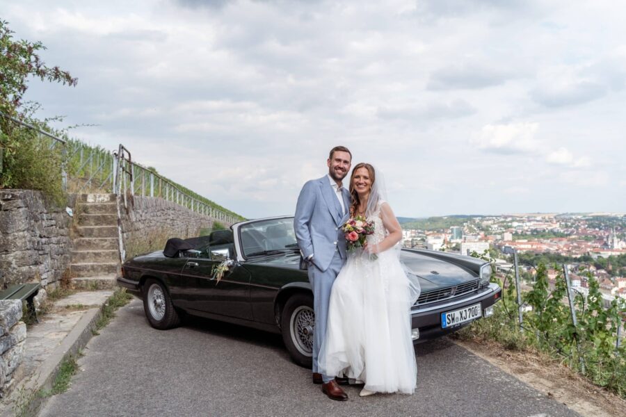 Hochzeit Steinburg Würzburg | Editorial Style & Party | Florian Knusper 58 Brautpaar vor Auto mit Stadtblick im Hintergrund