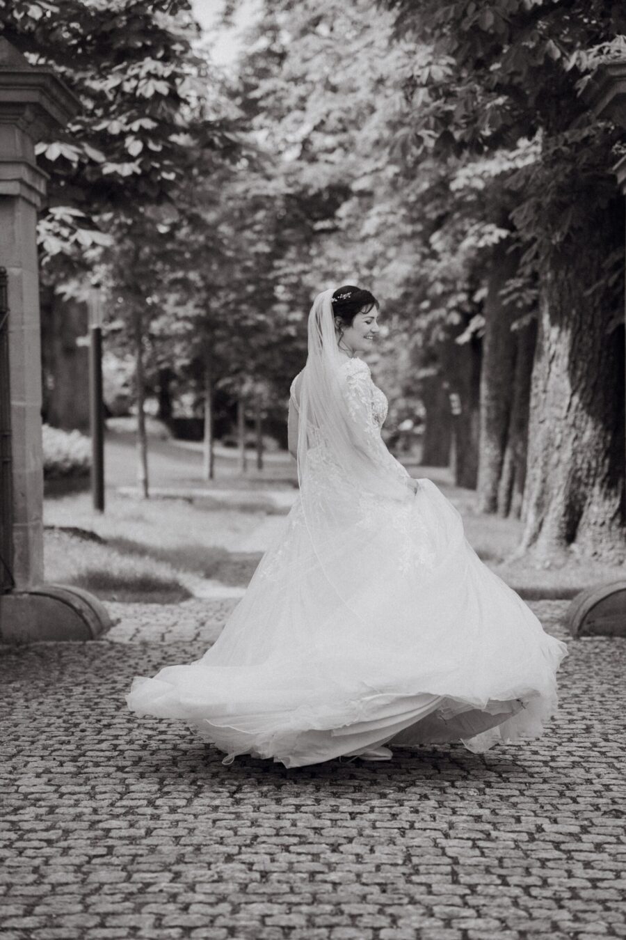 Braut im Hochzeitkleid auf gepflastertem Weg im Park.
