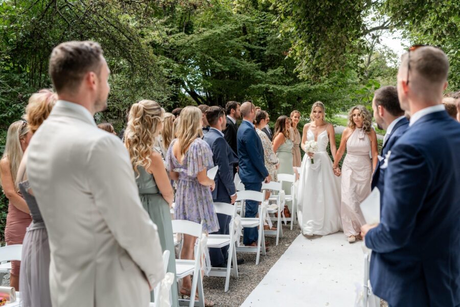 Hochzeit Villa Oriental | Editorial Summer Vibes & Live Cooking 370 Braut schreitet Hand in Hand durch Gartenallee