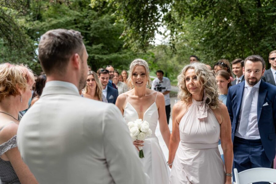 Braut mit Strauß bei Outdoor-Trauung mit Gästen.