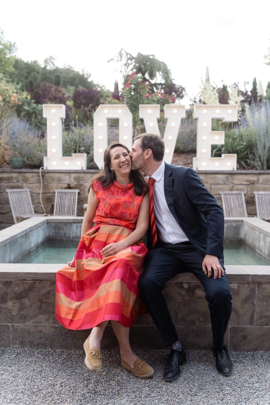 Paar sitzt vor großem LOVE-Schild im Garten.