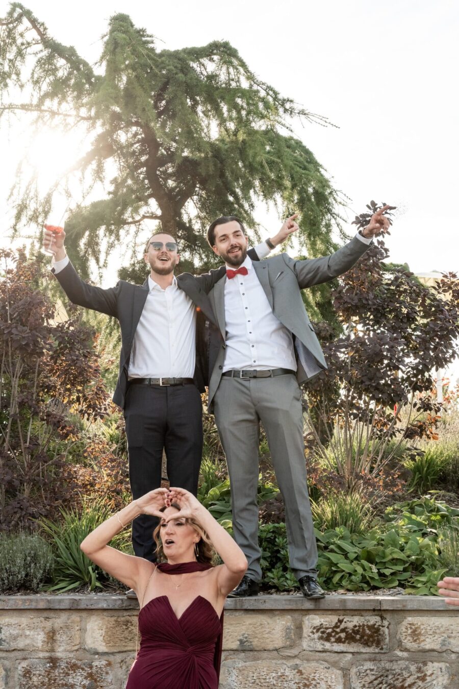 Hochzeitsgäste feiern im Garten vor großer Tanne.