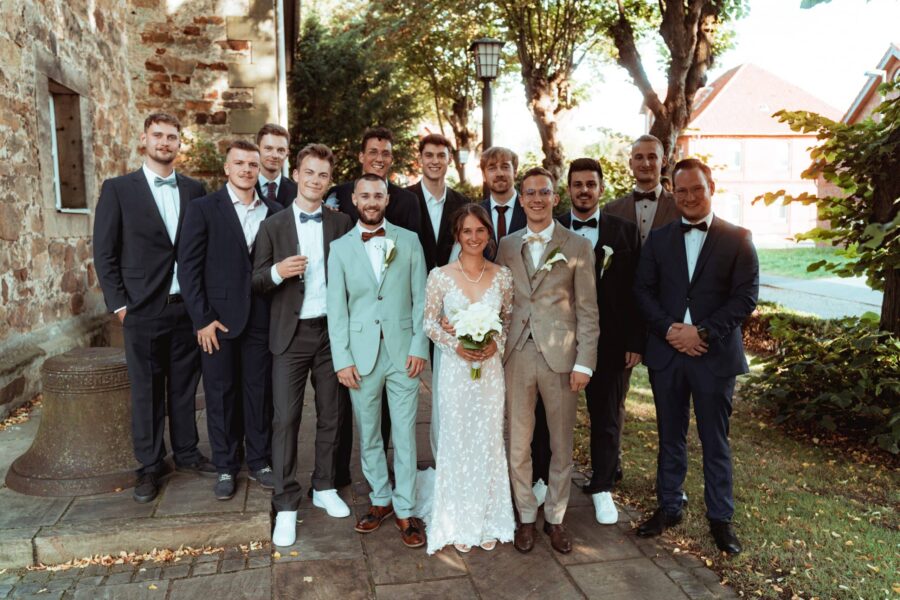 Brautpaar und Gäste vor Backsteinmauer im Garten