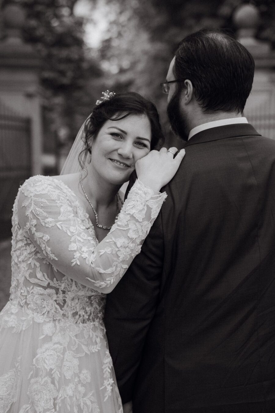 Braut im Spitzenkleid lehnt sich an Bräutigam im Anzug