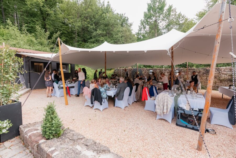 Gäste feiern unter Zeltdach im Garten bei Hochzeit.