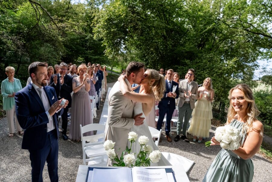 Brautpaar küsst sich vor applaudierenden Hochzeitsgästen