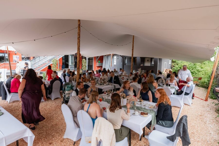 Hochzeitsgäste beim Essen im überdachten Außenbereich