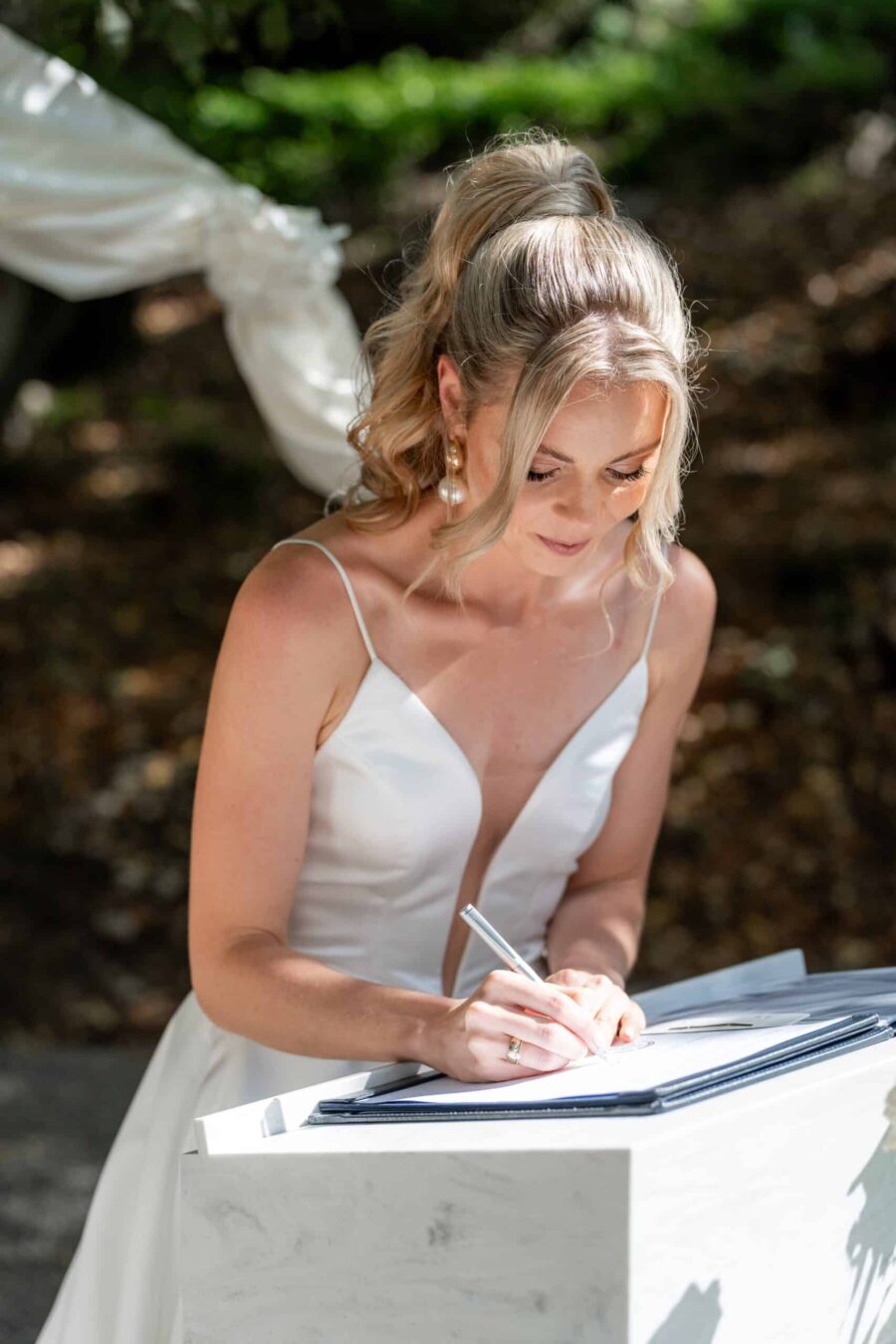 Braut unterschreibt Hochzeitsurkunde im Freien.