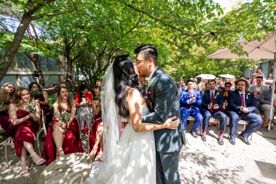 Brautpaar küsst sich vor applaudierenden Gästen im Garten