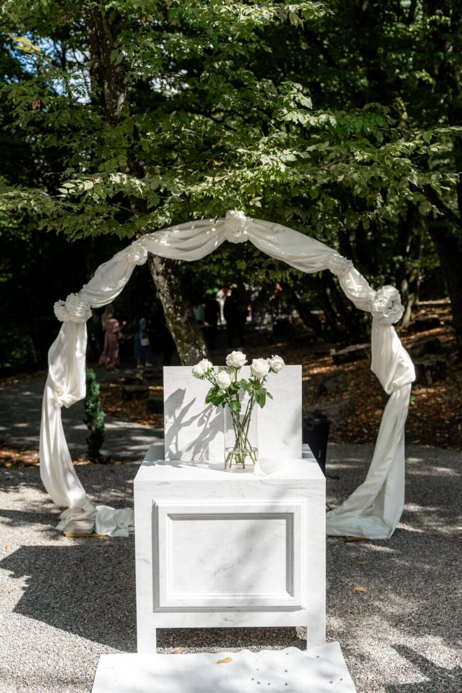 Hochzeitsaltar mit Blumen und weißem Stoffbogen im Freien.