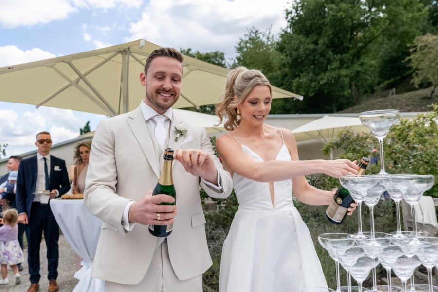Brautpaar füllt Champagnerturm im Garten.